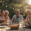 A diverse, multigenerational group of people laughing and sharing a meal together outdoors, representing the health benefits of social connection and belonging.